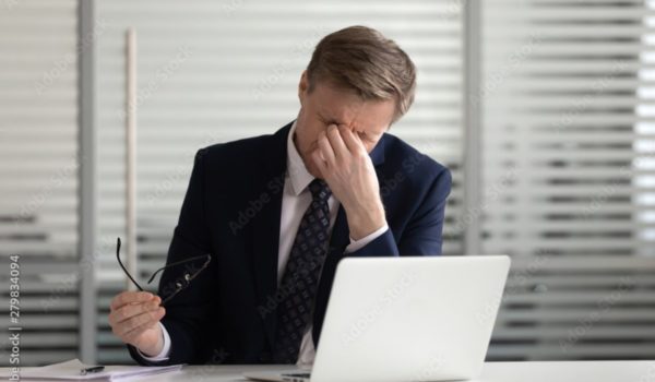 Man holding bridge of nose with eyes closed, sitting at a computer.